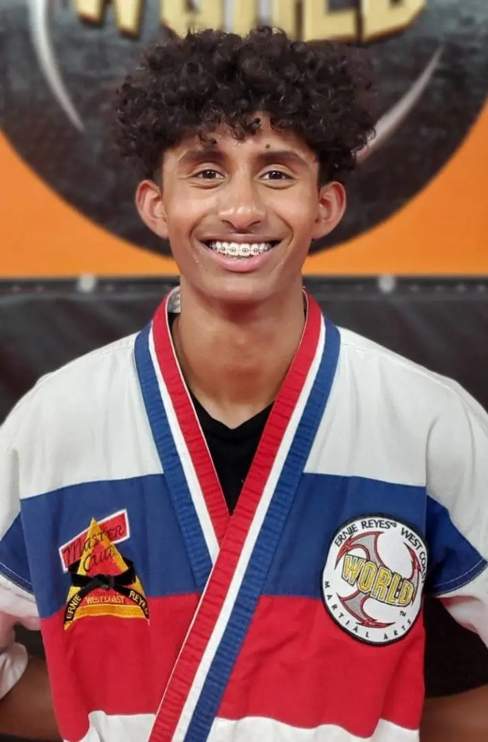 A young man in a karate outfit smiling for the camera.