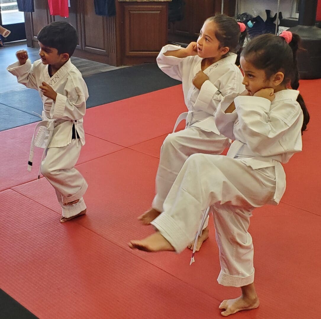 A group of kids practicing martial arts on a red mat.