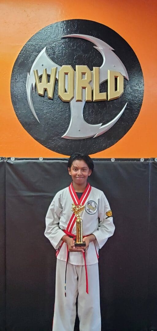 A young boy is holding his trophy in front of the world sign.